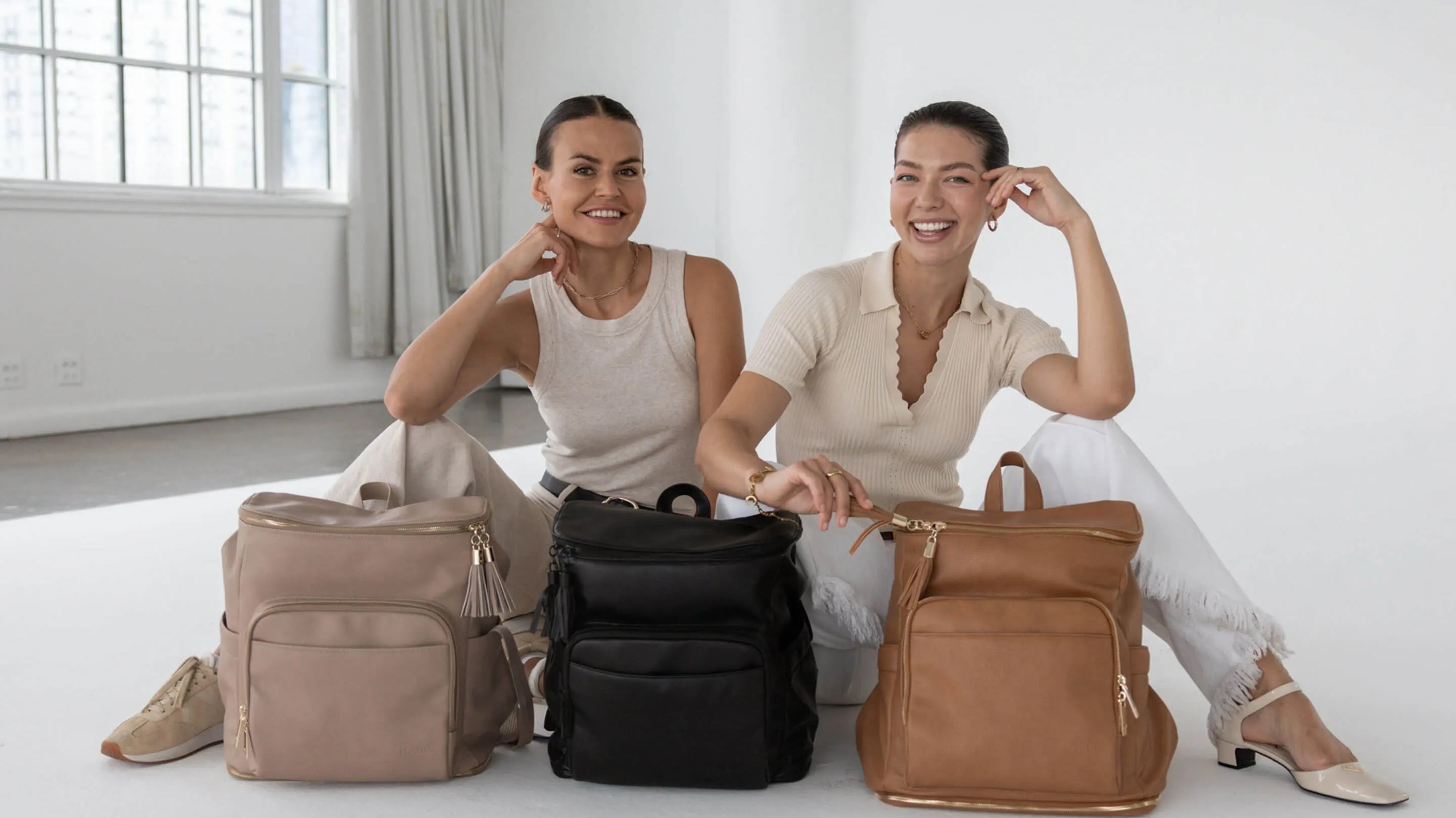 Two women sitting together with three different colours of nappy bags on display.