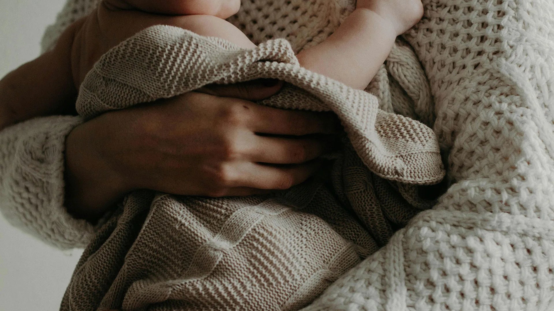 First-time mum holding her baby wrapped in a knitted swaddle – one of the best baby items 2025 for comfort and bonding