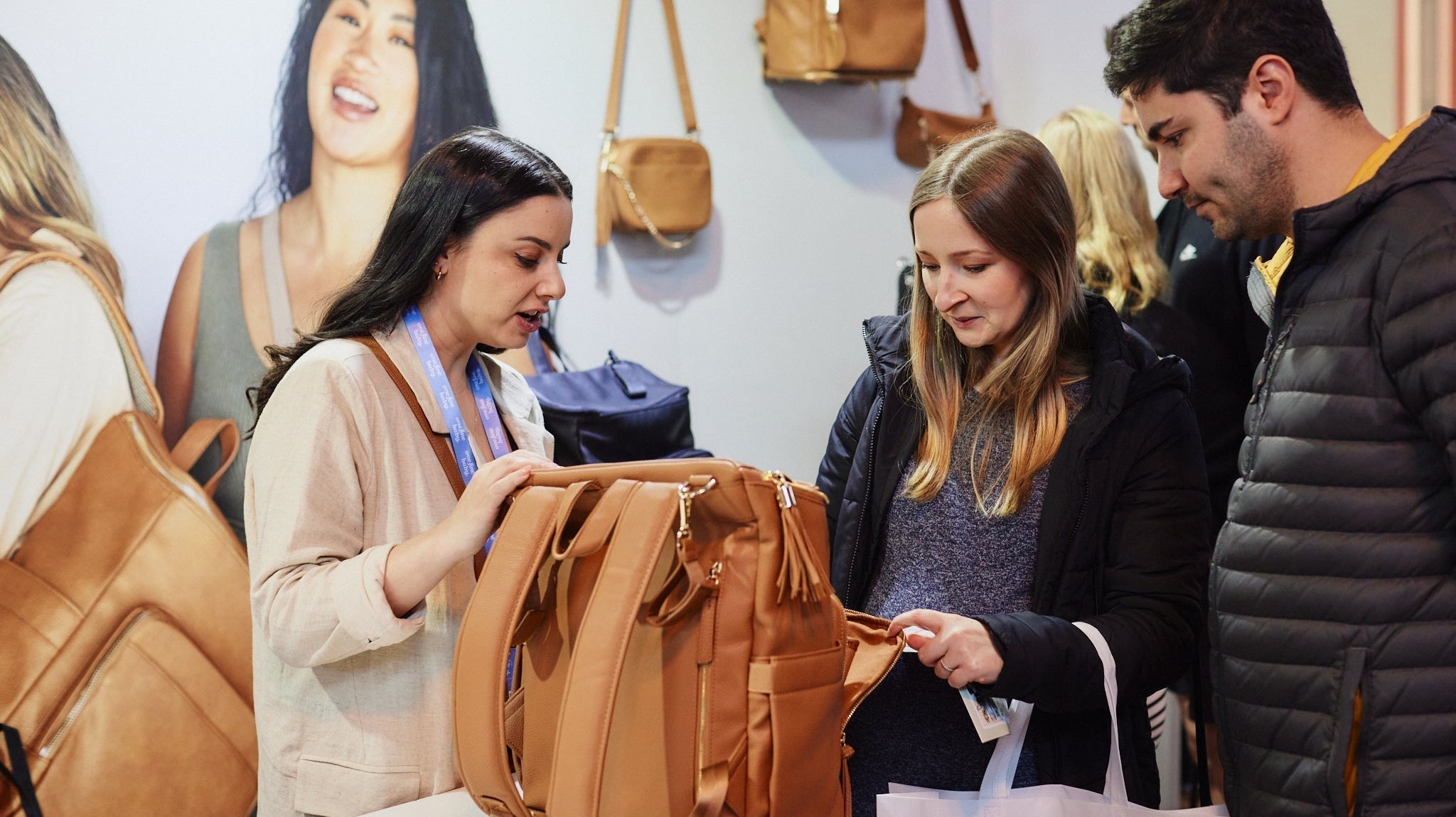 One woman exhibitor showing nappy bags to two visitors at a baby expo in Australia.