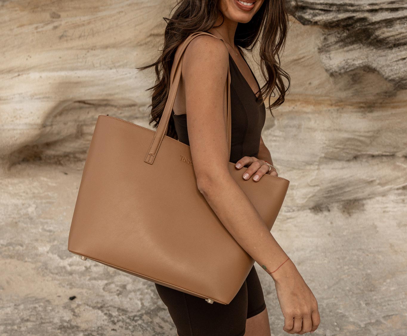 Professional woman in Australia wearing the best tote bag for work, a brown leather tote, while relaxing at the shore.