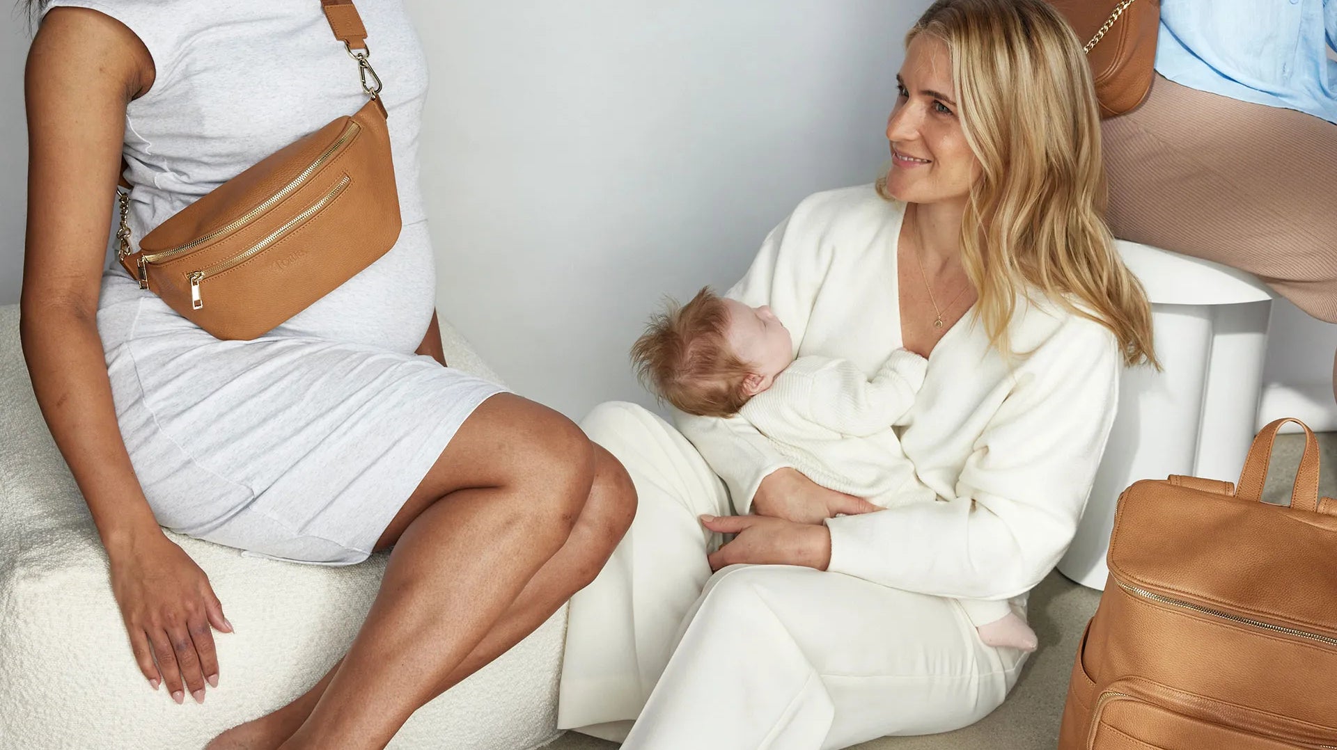 Two women on a white couch; one holds a baby, the other a purse, a baby shower gift nappy bag.