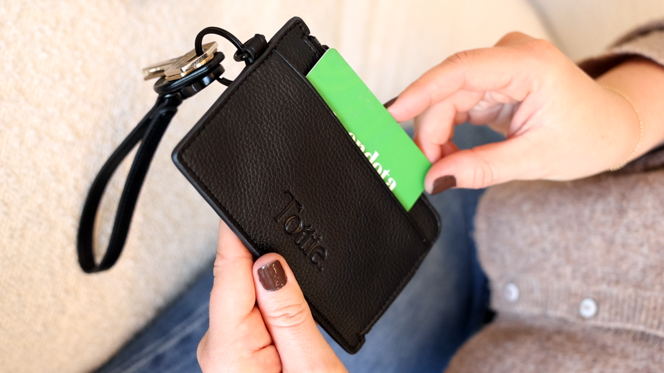 Closer look of a hand pulling a card from a black card holder wristlet wallet, highlighting card holder wallet vs wallet features