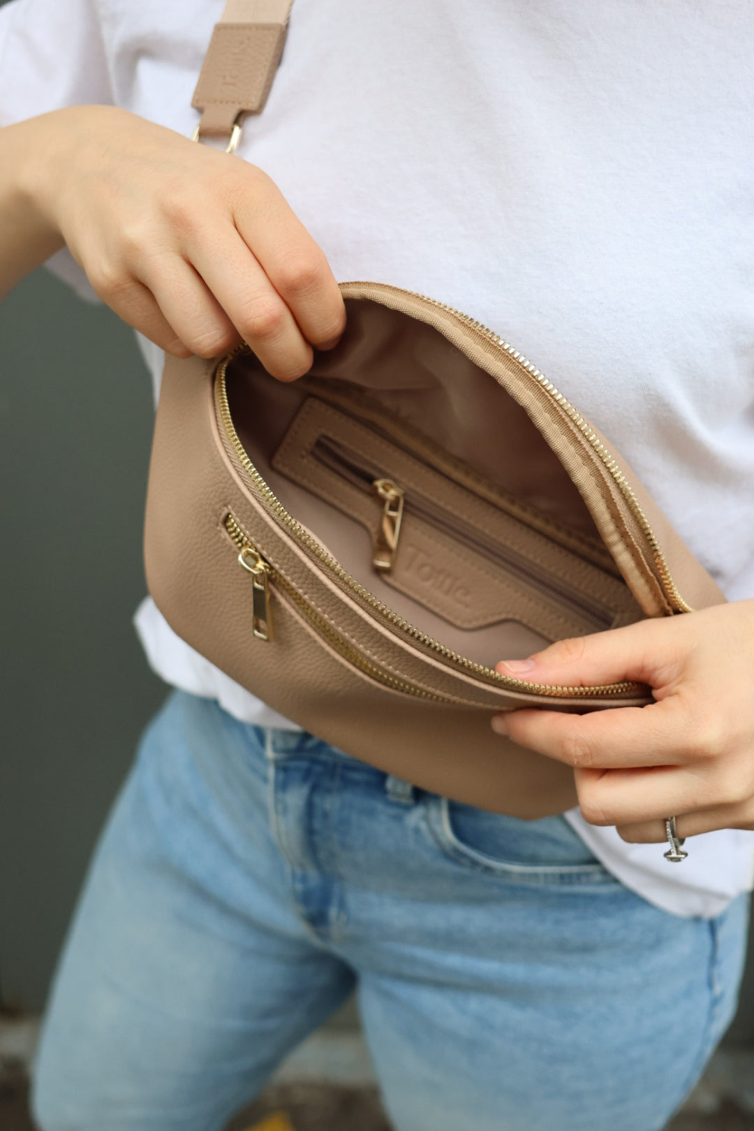 A woman dressed in a white shirt and jeans carries a black bum bag