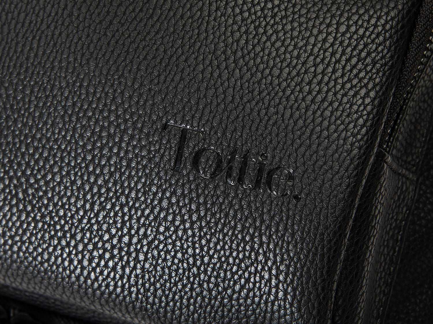 A black leather travel backpack with black zippers and has Tottie marking on it