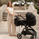Black nappy bag backpack with black hardware attached to a pram using pram clips.