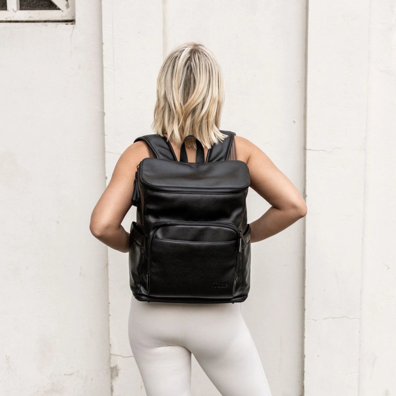 Back view of a woman with a functional black travel backpack with matching black hardware.