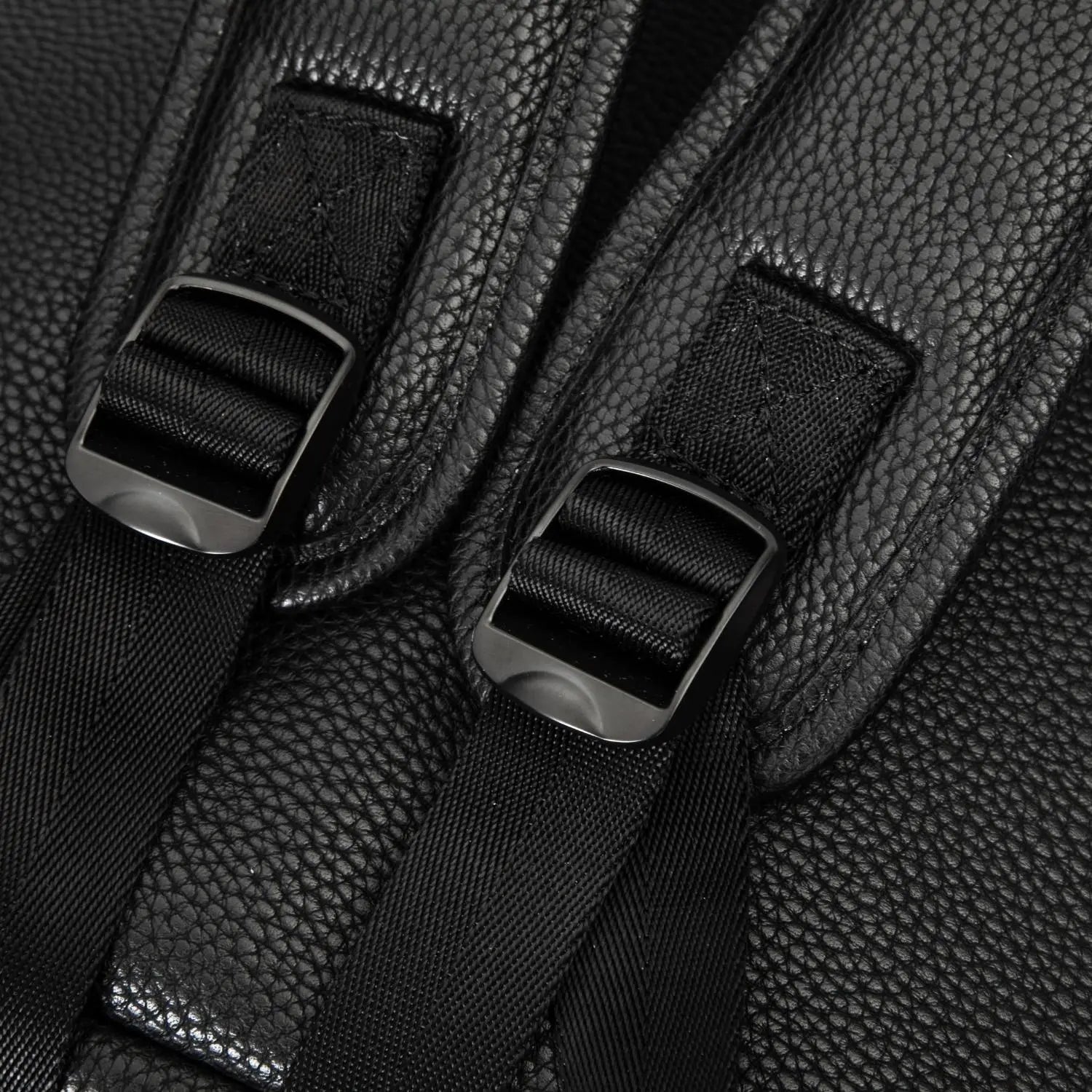 A close-up of the strap hardware on a black nappy bag backpack, featuring tonal black hardware, photographed on a white background.