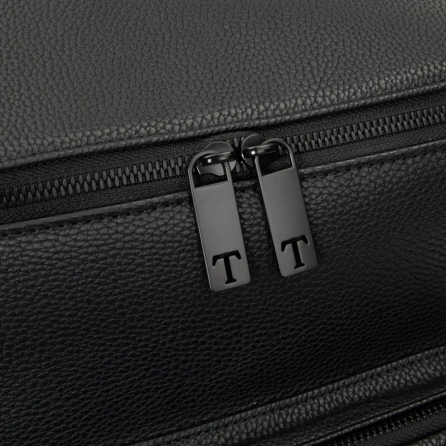 Detailed view of T-shaped zipper pull on black nappy bag backpack with black hardware against white background