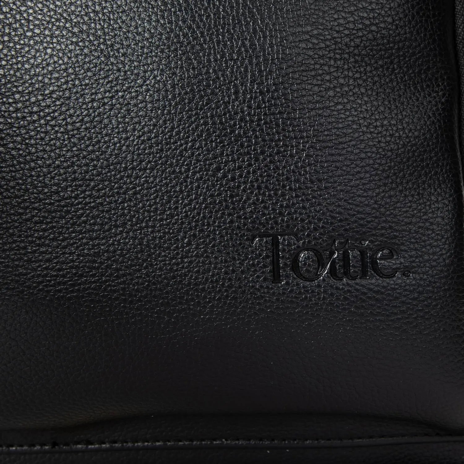 Close-up of embossed Tottie logo on black nappy bag backpack with gold hardware – premium branding detail.