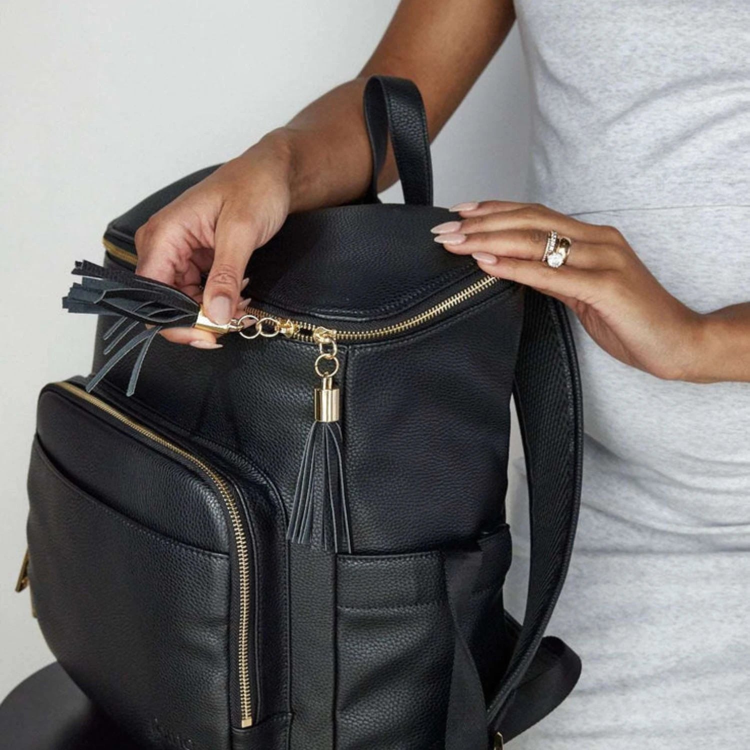 Pregnant woman holding a black nappy bag backpack with elegant gold hardware, shown in close-up.