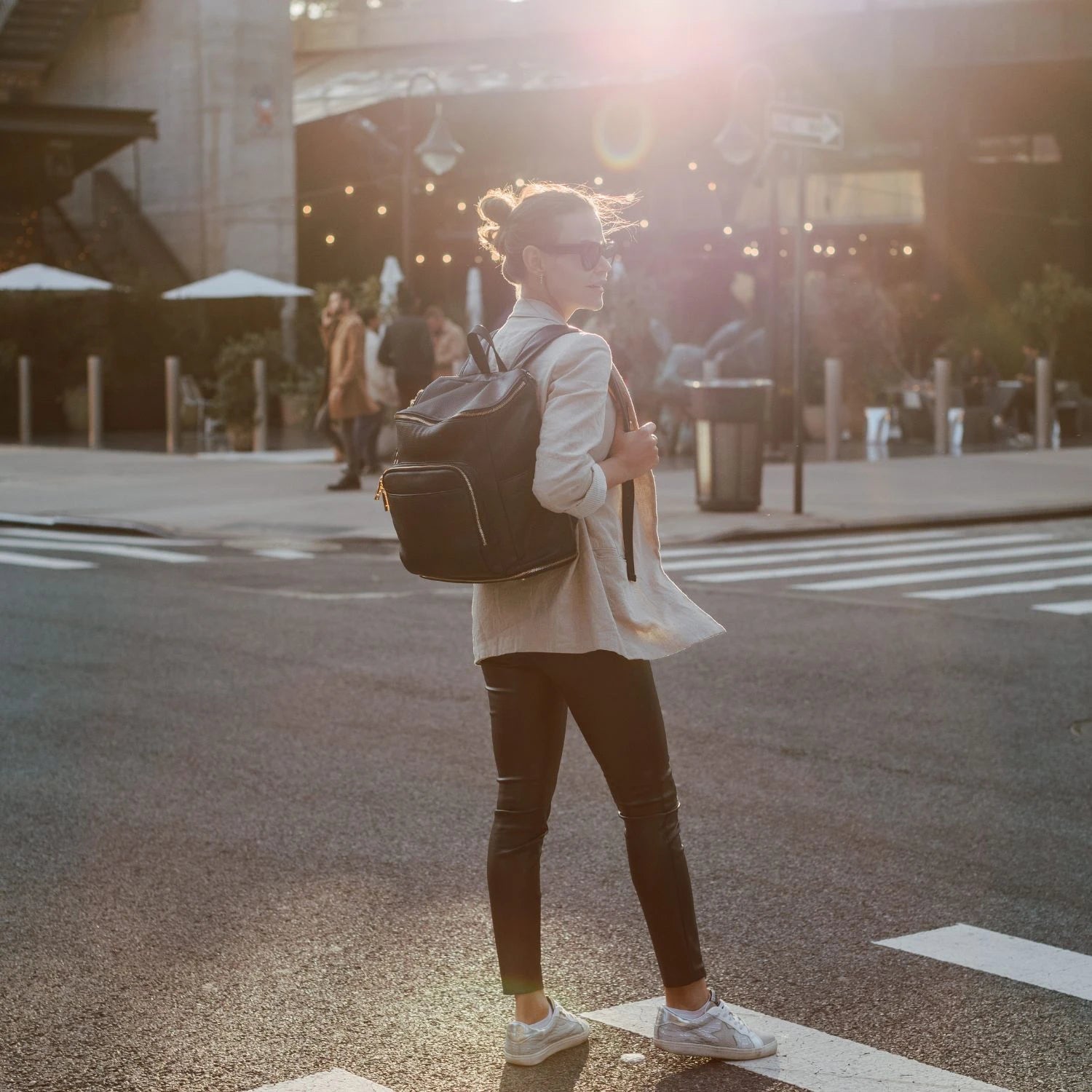 Back view of a woman carrying a black backpack with gold hardware during a sunset