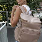 Woman seen from behind carrying a stone nappy bag backpack with gold hardware on her back shoulder