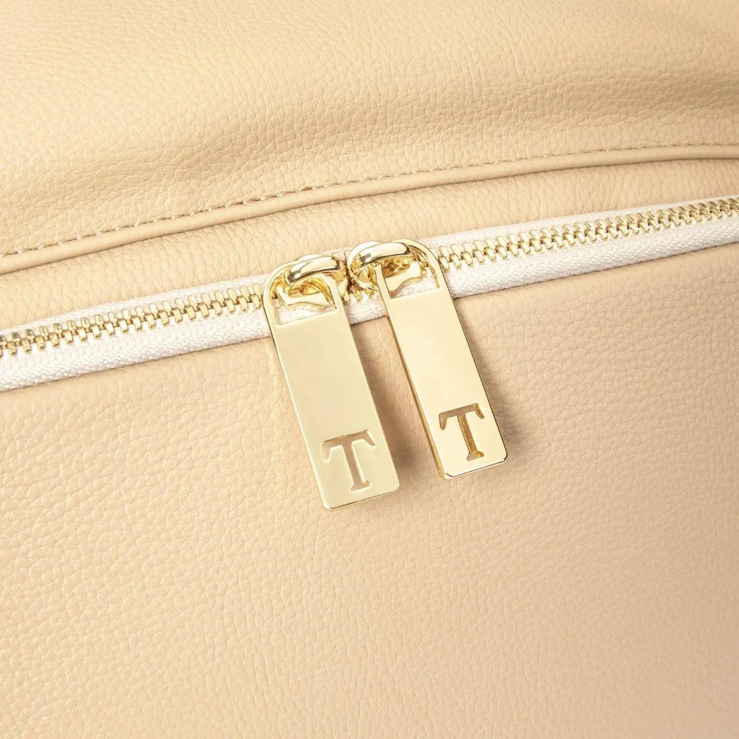Detailed view of gold Tottie zipper with T emblem on stone colour nappy bag backpack – stylish and functional accent.
