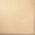 Detailed view of Tottie logo embossed on stone colour nappy bag backpack with gold hardware – elegant brand touch