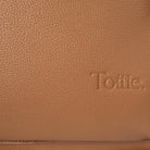 Close-up of embossed Tottie logo on tan nappy bag backpack with gold hardware – premium branding detail.