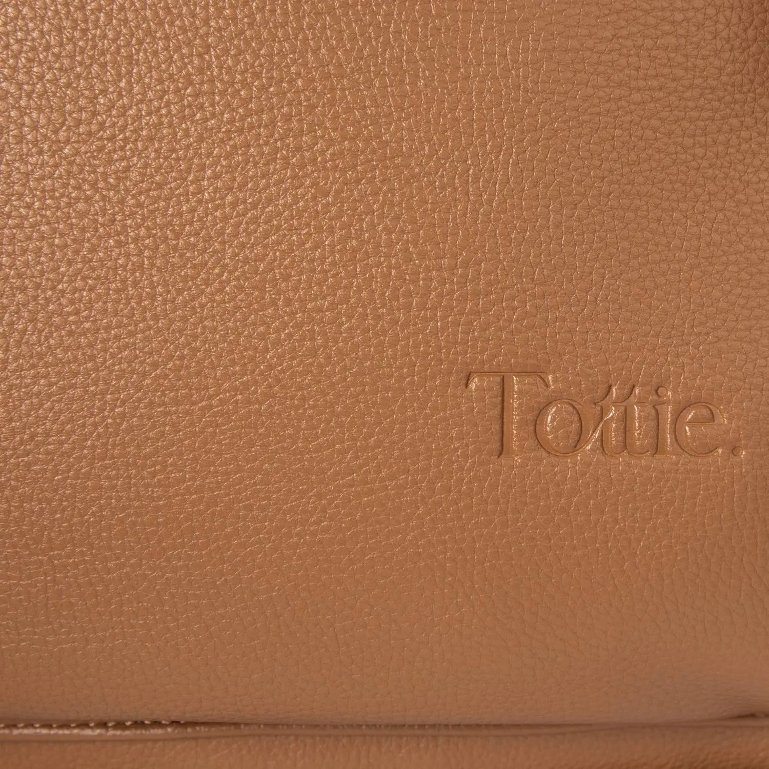 Close-up of embossed Tottie logo on tan nappy bag backpack with gold hardware – premium branding detail.