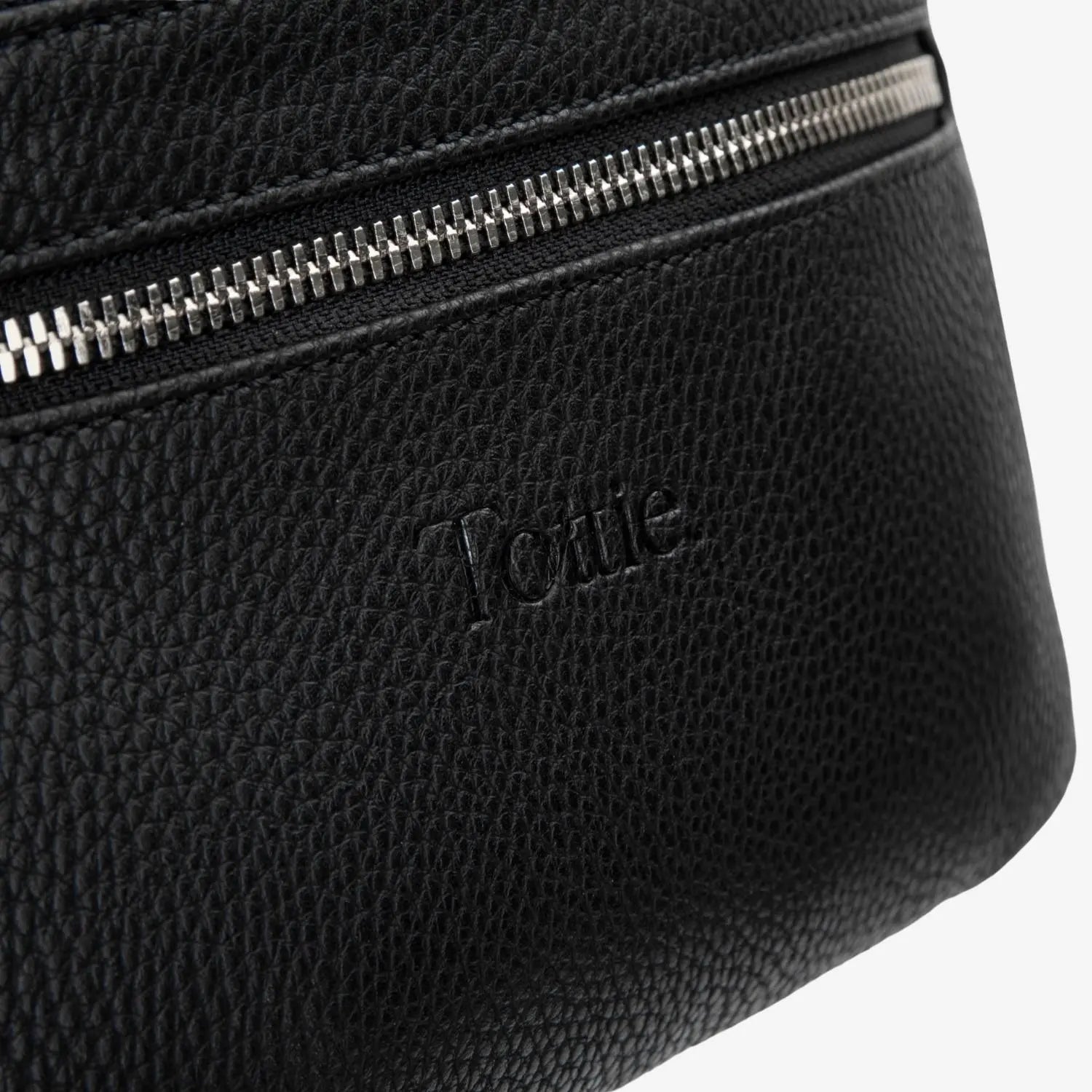 Tottie logo embossed on black bum bag close-up with polished silver hardware accents.