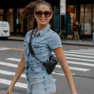 Street-style shot of a woman in a denim romper styling a black bum bag with black hardware.