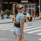 Casual street fashion – woman pairs a denim romper with a sleek black bum bag featuring black hardware