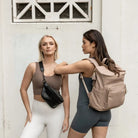 Two women in casual summer outfits – one wearing a black bum bag with black hardware, the other carrying a stone backpack with gold hardware.