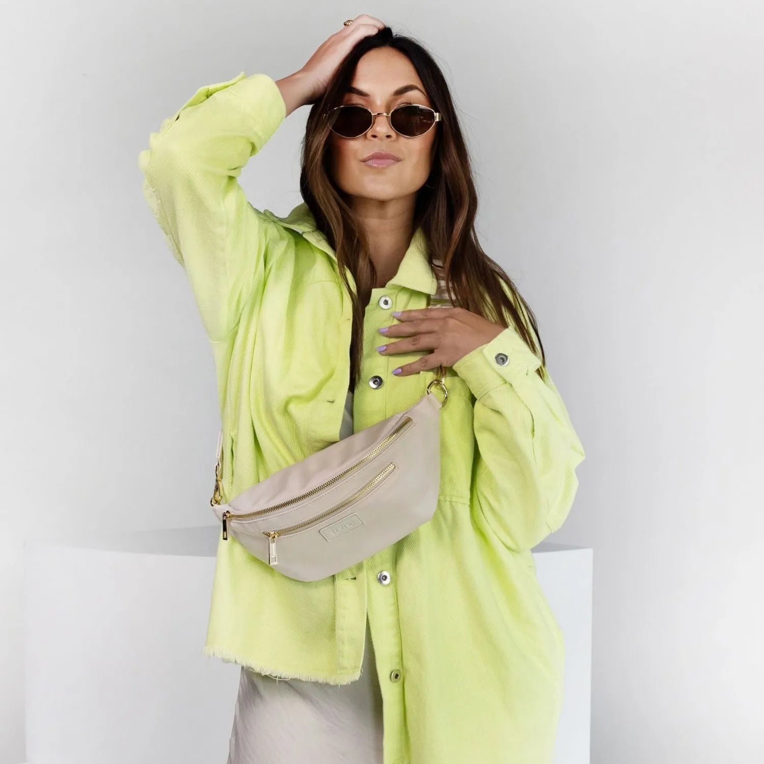 Woman wearing yellow-green coat and stylish nylon bum bag posing confidently.
