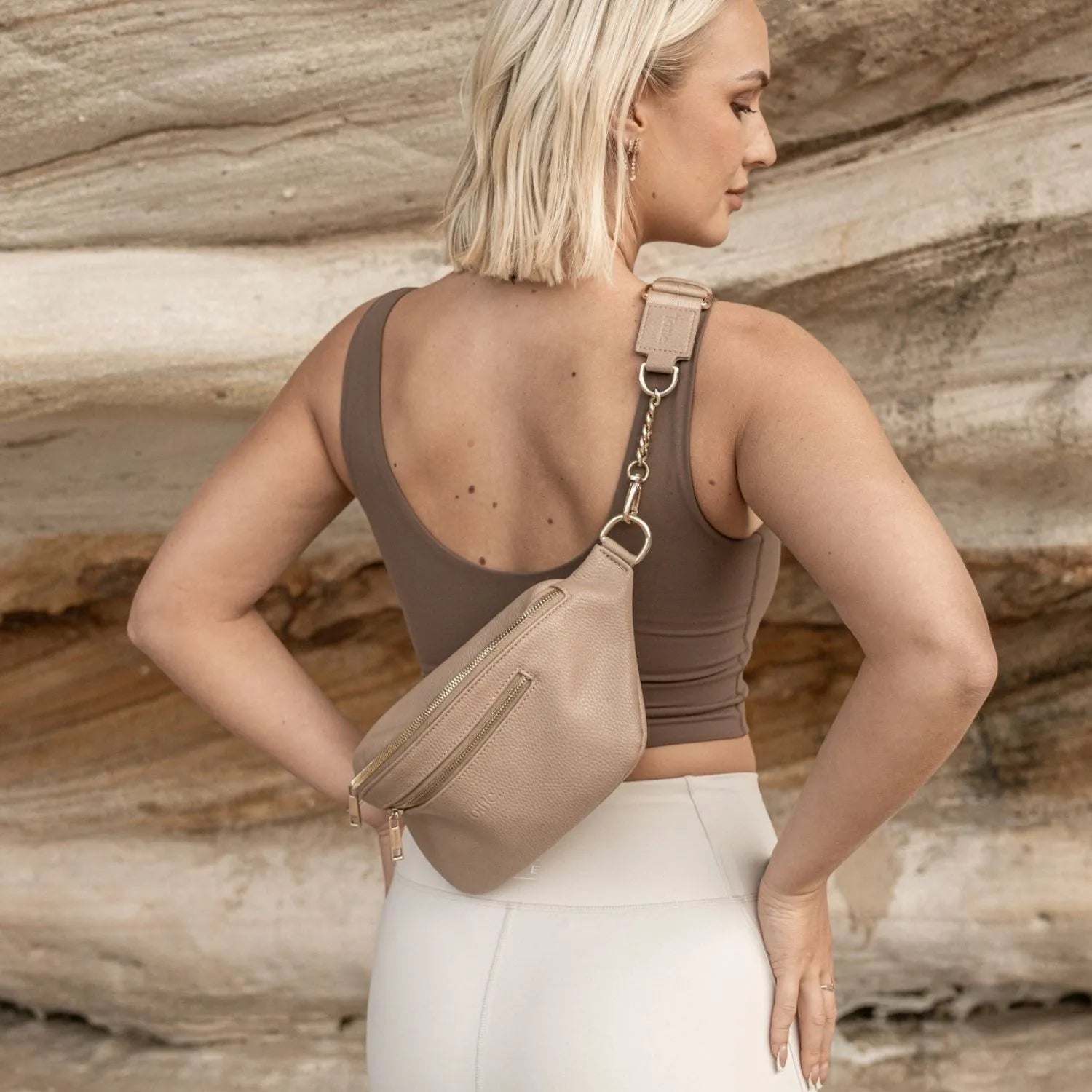 Back view of a woman carrying a stone crossbody bum bag with gold hardware, styled with summer clothing