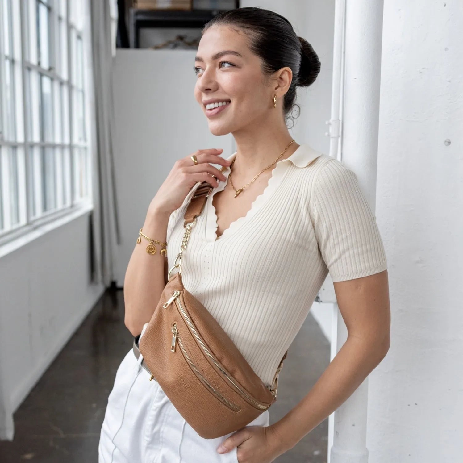 Smiling woman wearing tan bum bag with gold hardware in crossbody style.