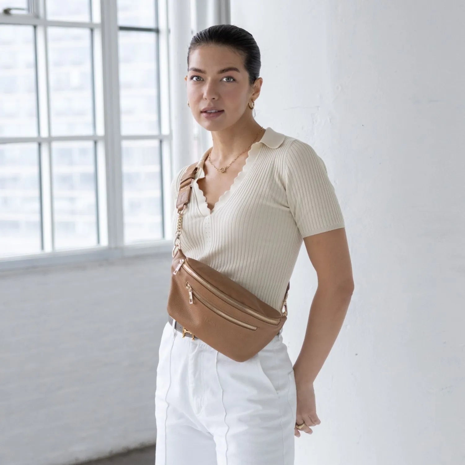 Woman wearing a tan bum bag with gold hardware crossbody style at the front for easy access and hands-free convenience.
