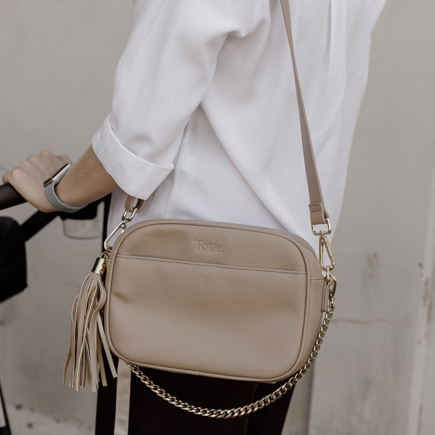 Beige crossbody bag with chain detail worn by a woman in a white top.