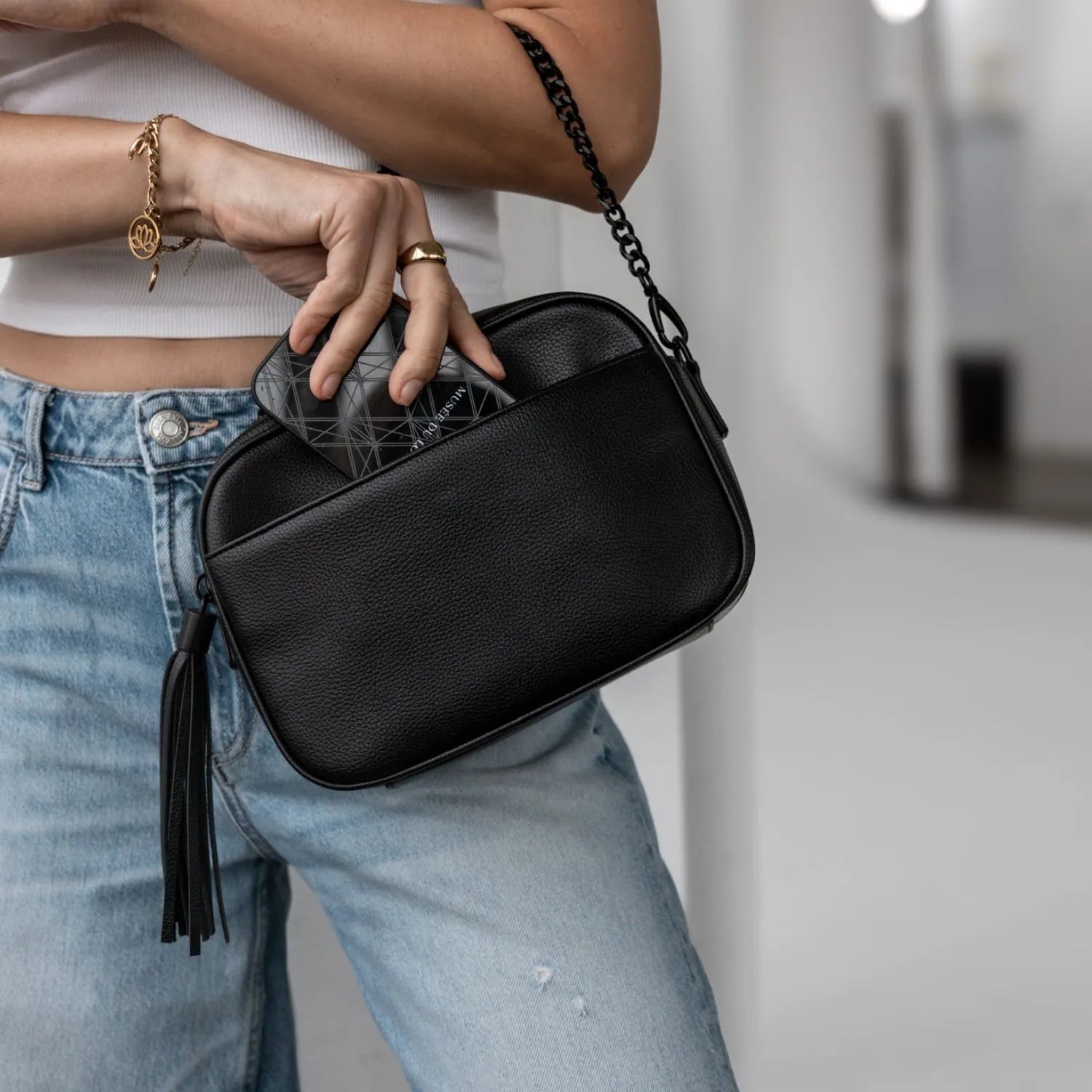 Close-up of a woman placing her phone inside a black crossbody bag with black hardware.