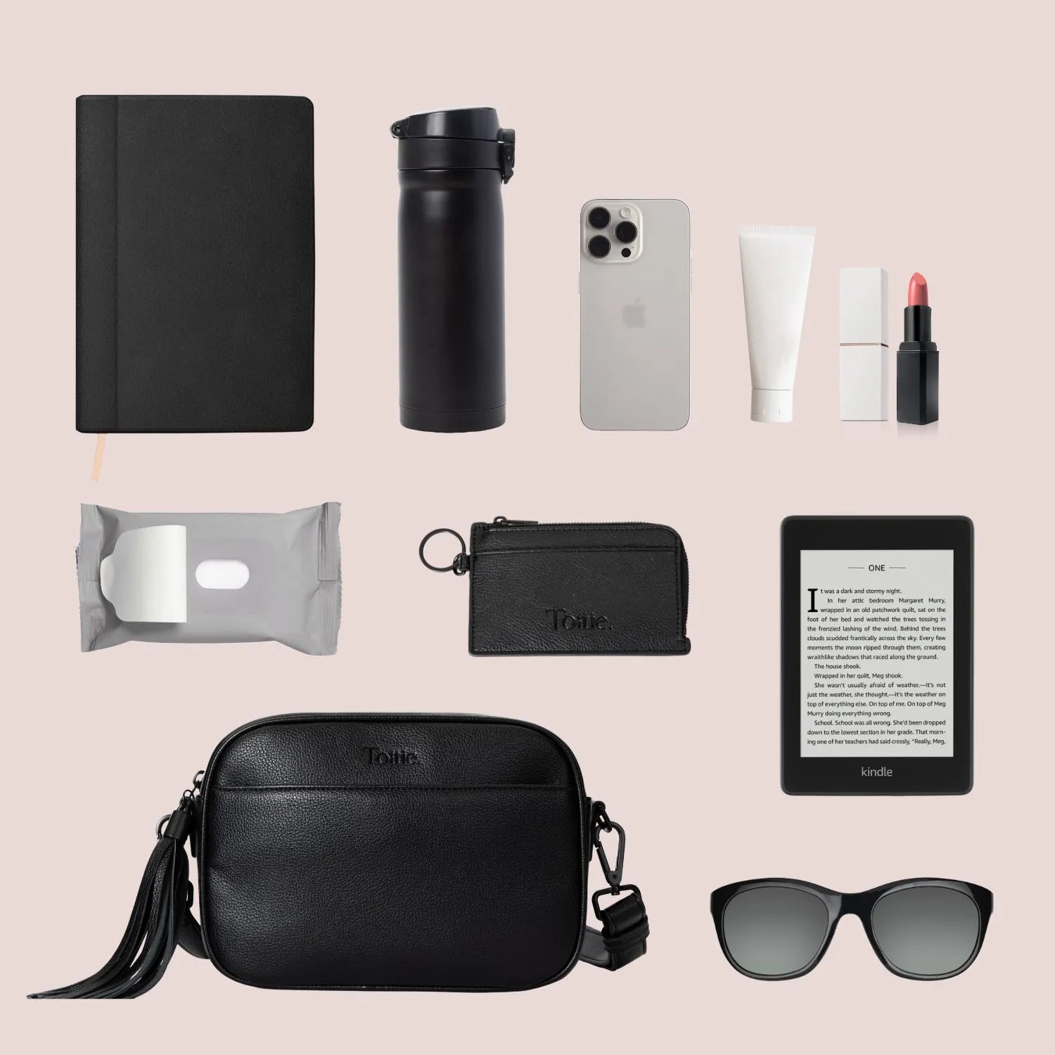 Women's essentials laid out with a black crossbody bag featuring phone, water bottle, Kindle, and wallet.