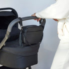 Black crossbody bag strap fastened to black stroller for easy carrying.