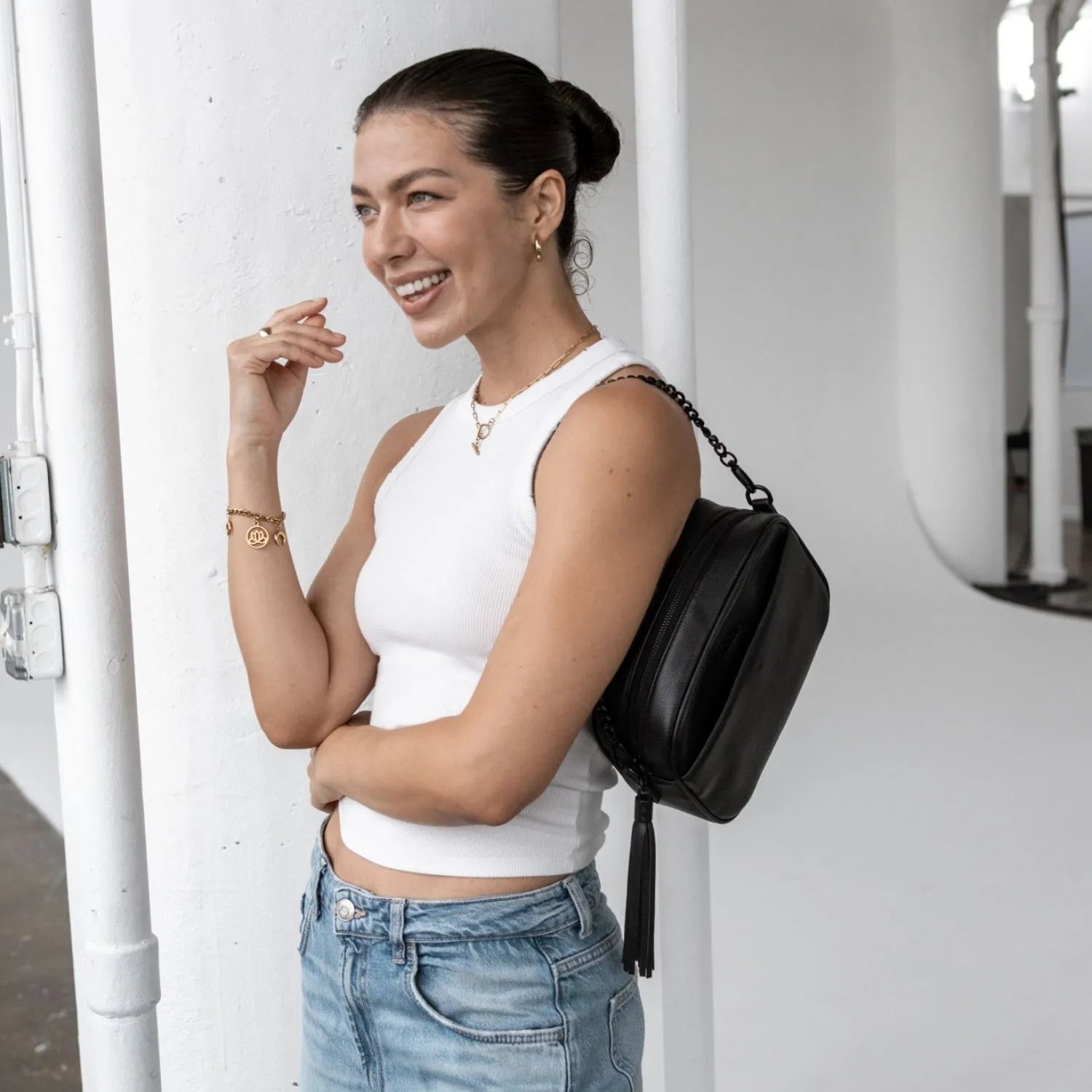 Woman wearing white top carrying a black crossbody bag with black hardware on her shoulder.