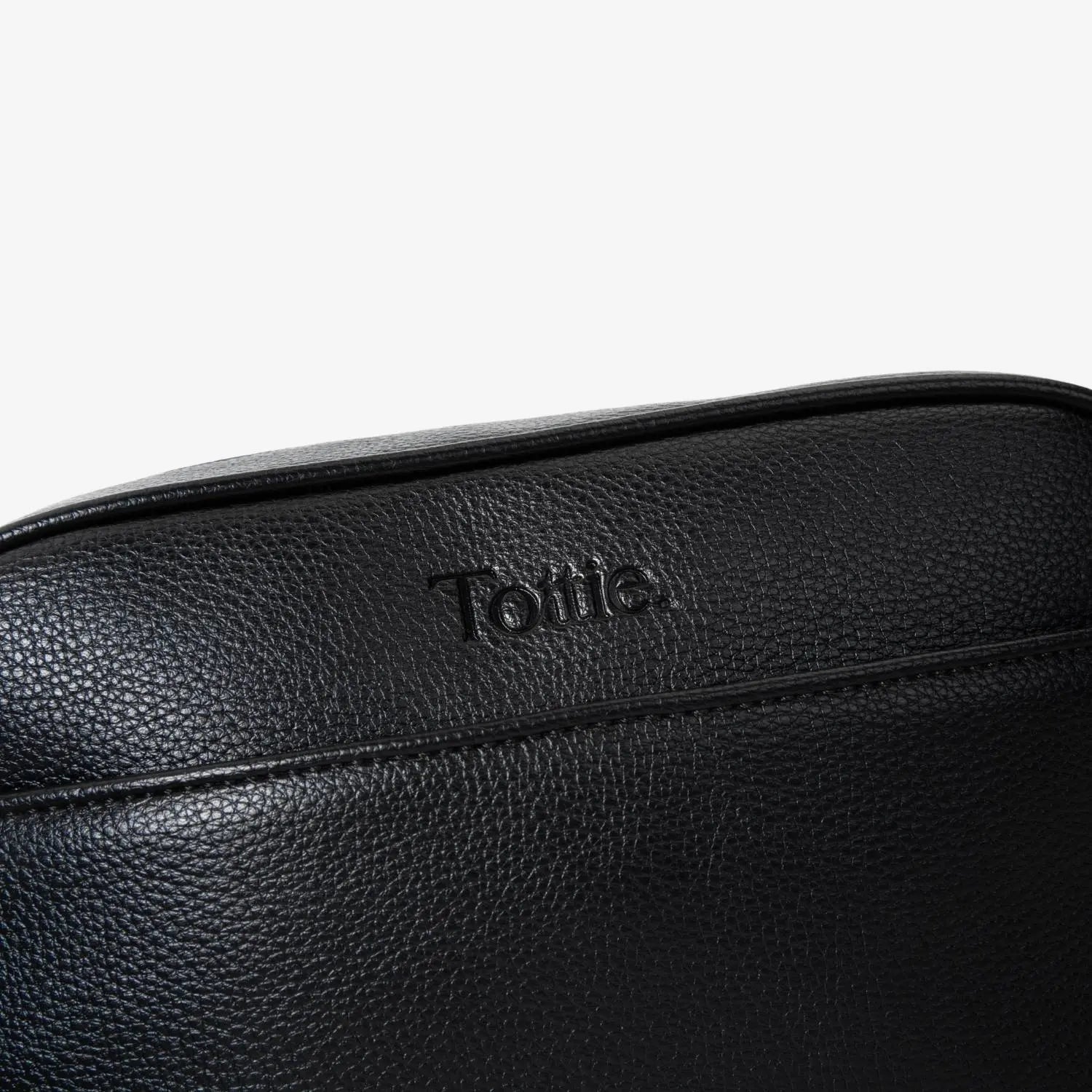 Detailed view of Tottie logo embossed on black crossbody bag featuring silver hardware accents