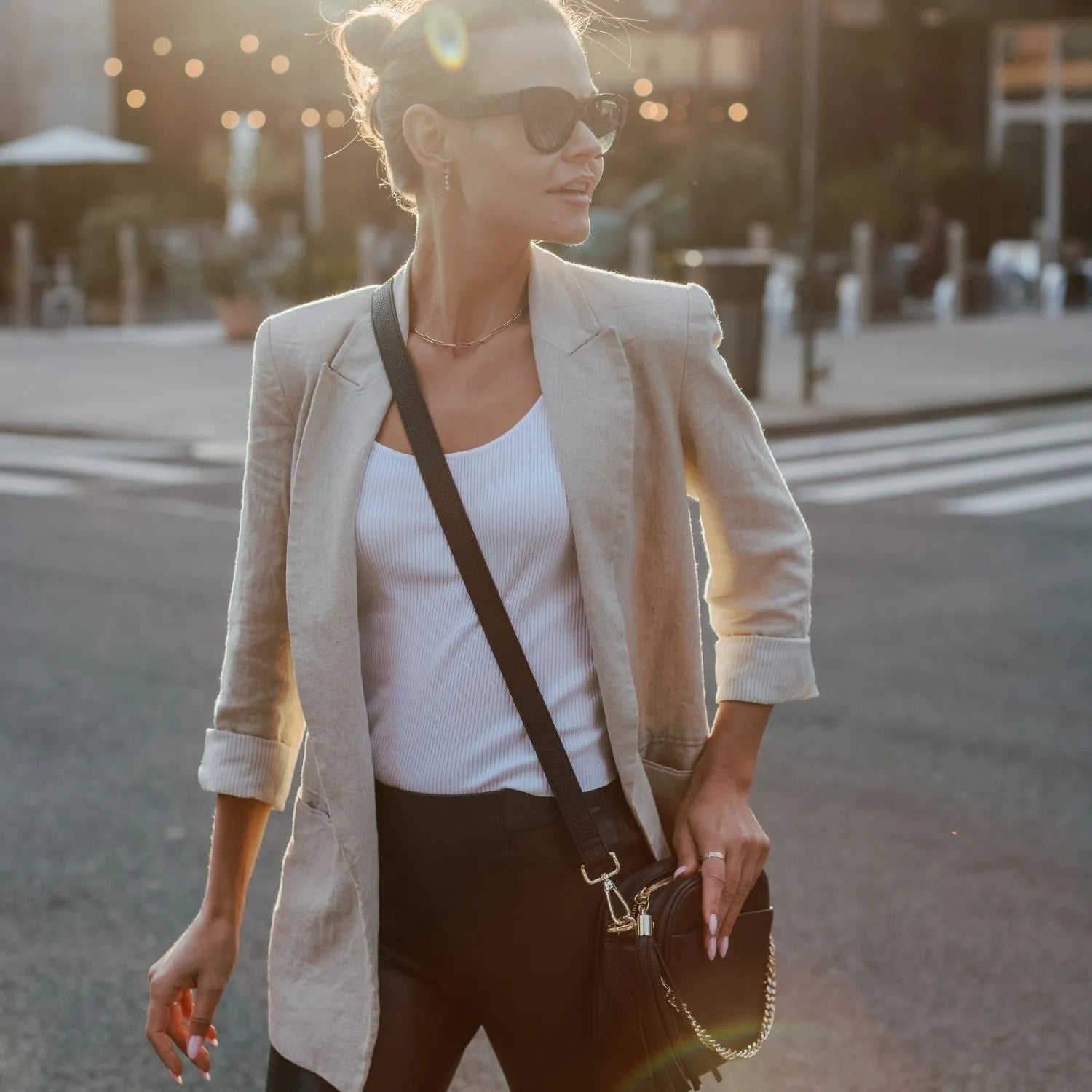 Black crossbody bag with gold hardware carried by woman wearing shades.
