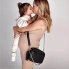Woman with black crossbody bag with silver hardware lovingly holding and kissing her baby.