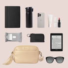 Elegant crossbody bag in stone with gold detailing surrounded by daily essentials like makeup, notebook, and lotion