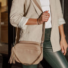 Detailed view of stone colour crossbody bag worn on shoulder by woman.