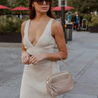 Stone colour crossbody bag carried on arm by woman dressed in dress.