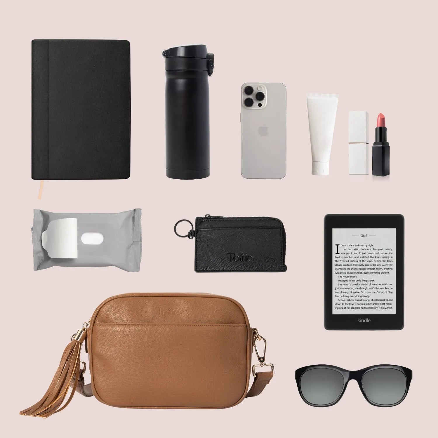 Crossbody bag in tan with gold hardware alongside makeup, Kindle, water bottle, and wallet.