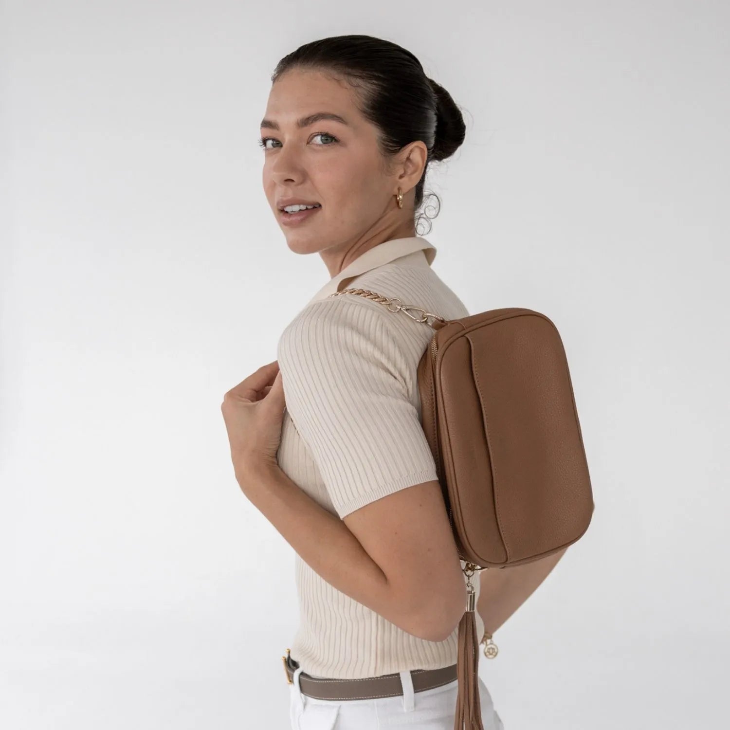Elegant woman holding tan colour crossbody bag with gold hardware in simple outfit.