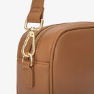 Close-up of gold hardware attached to tan colour strap of tan colour crossbody bag with gold hardware.