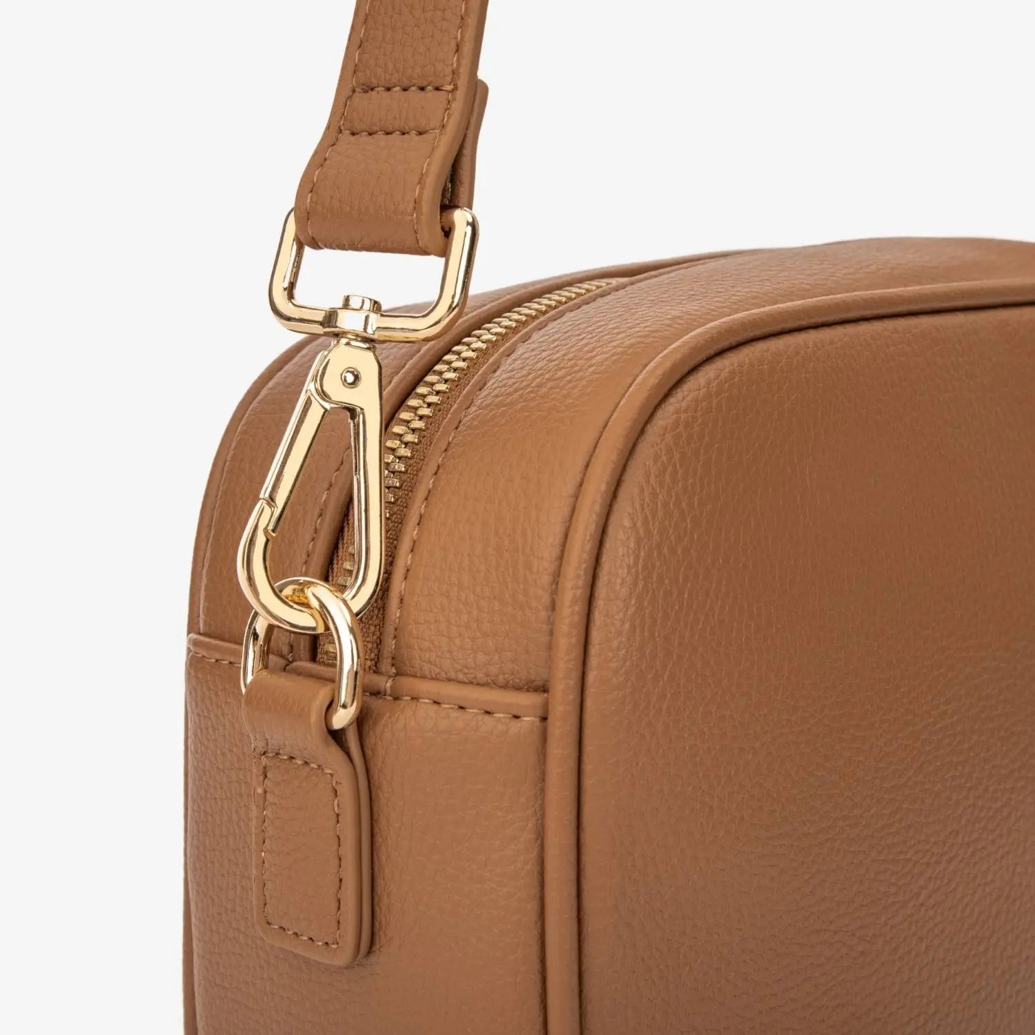 Close-up of gold hardware attached to tan colour strap of tan colour crossbody bag with gold hardware.