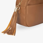 Bag tassel detail of tan colour crossbody bag accented with gold hardware