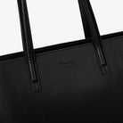 Detailed close view of Tottie logo embossed on black tote bag with textured surface.