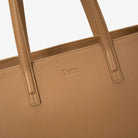 Detailed view of embossed Tottie logo on tan tote bag, highlighting brand authenticity.