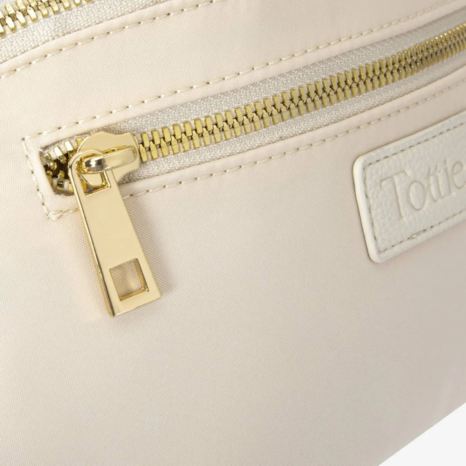 Close-up of bag zipper with embossed Tottie logo on cream nylon bum bag against white background