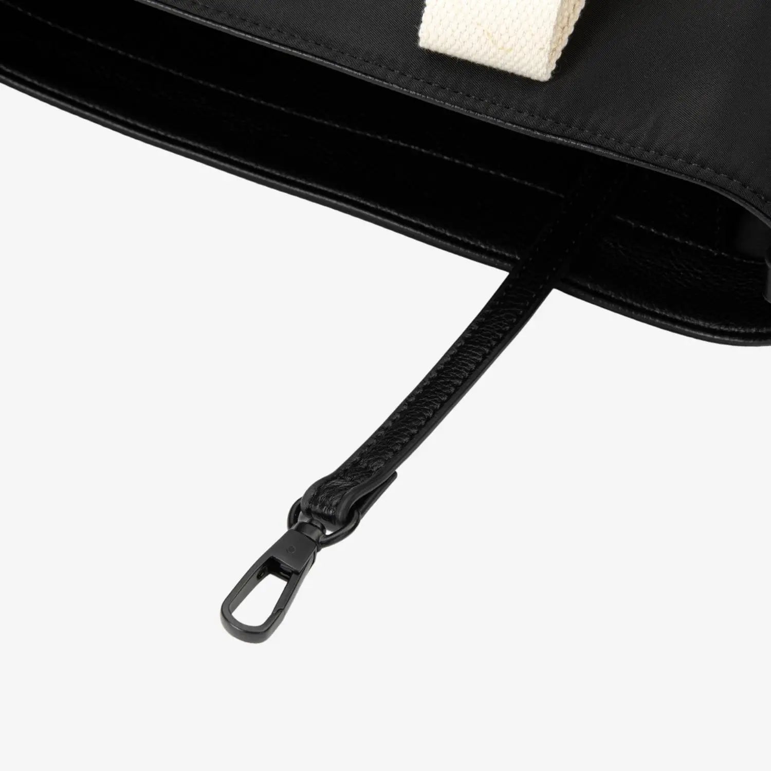 Detailed shot of matte black hardware on black nylon tote bag, featuring contrast cream strap