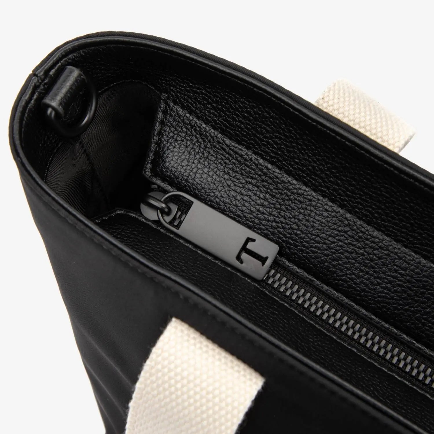 Close-up of zipper detail with T logo on black nylon tote bag with cream strap