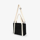 Slight side view of black nylon tote bag with cream strap on white background, showing bag shape and design.